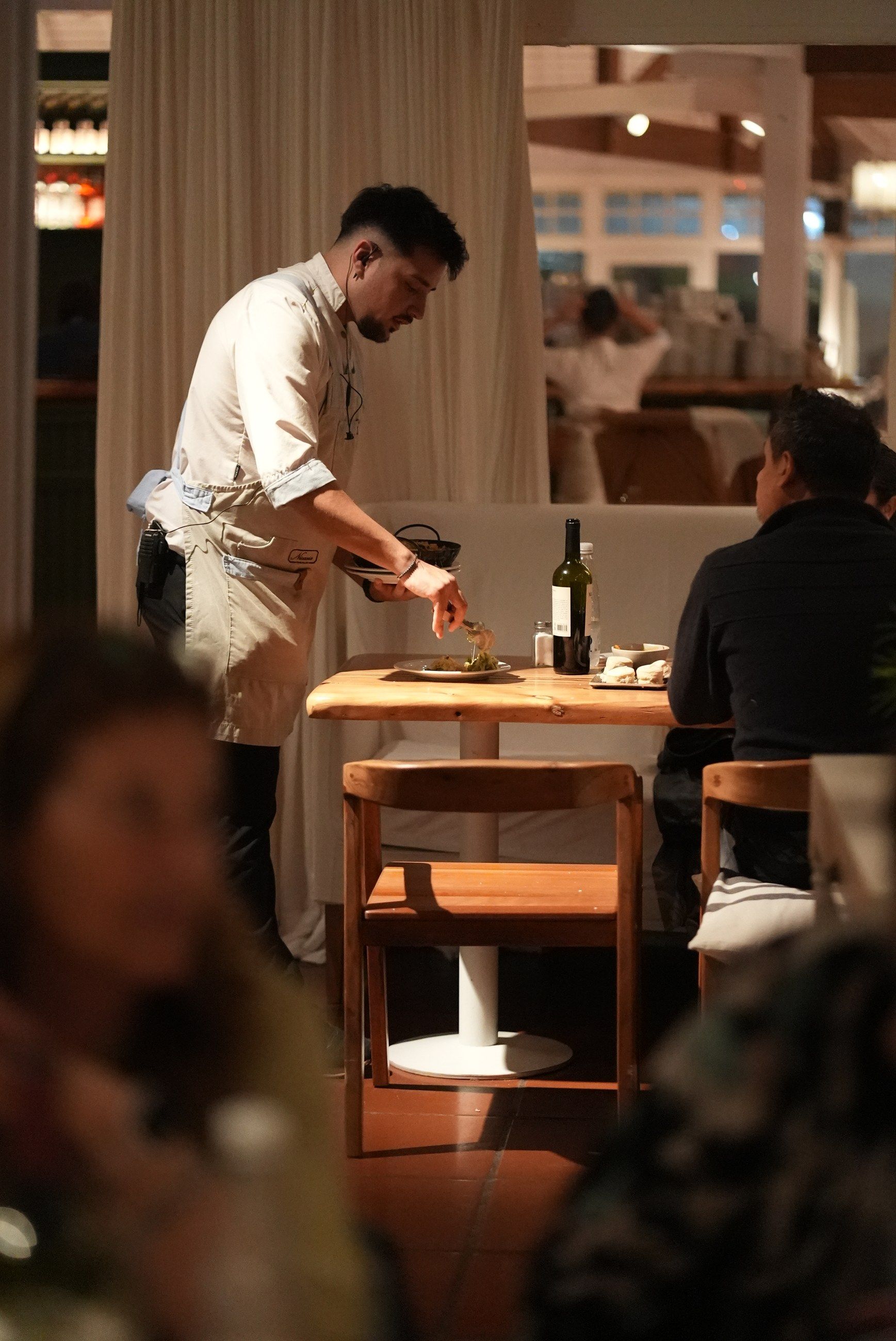 Un mozo detrás de la barra de madera, con la luz cálida del salón