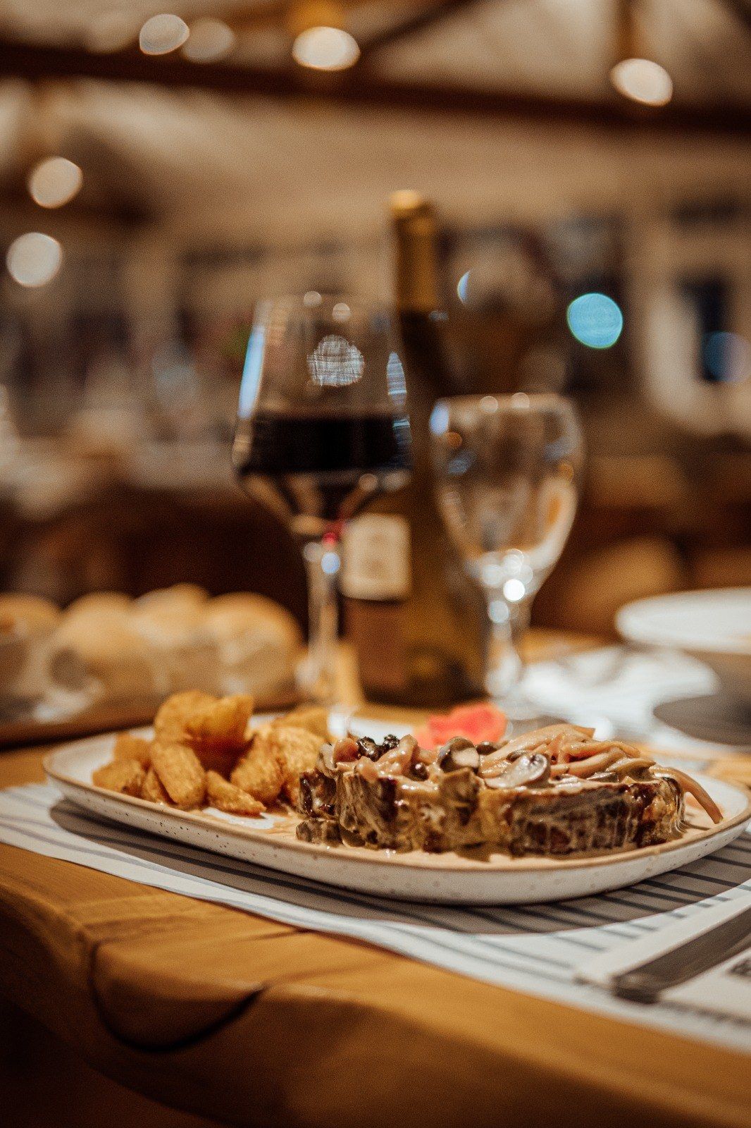 Bife con papas y hongos, con una copa de vino tinto y la botella detrás