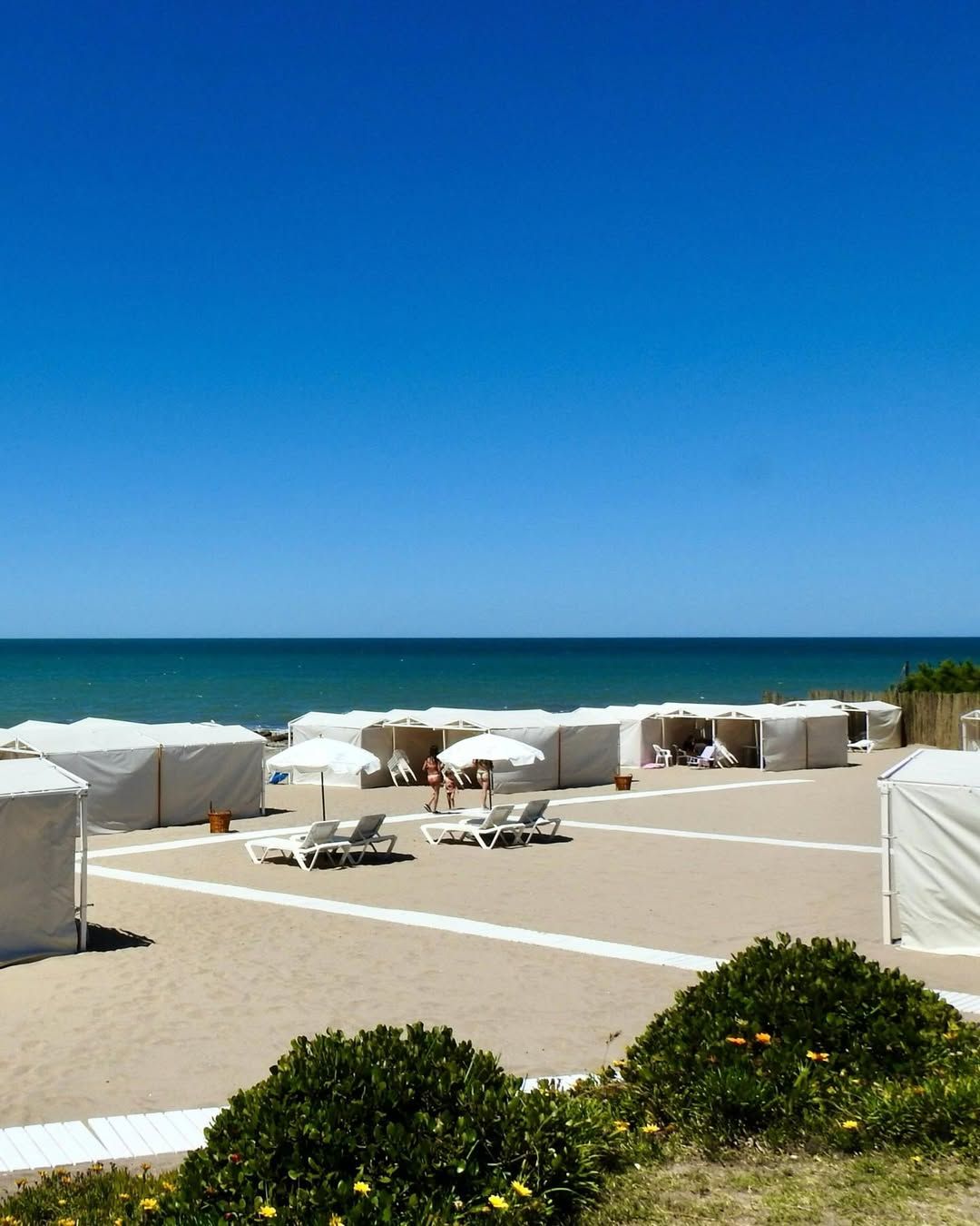 Las carpas blancas del balneario alineadas sobre la arena, con las reposeras, las sombrillas y el mar detrás