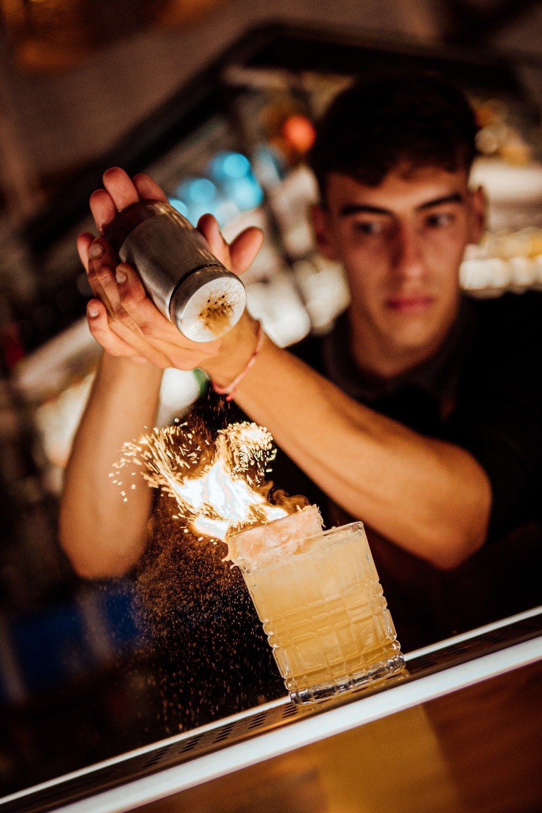 El bartender flameando un cóctel en la barra, con las chispas cayendo sobre el vaso
