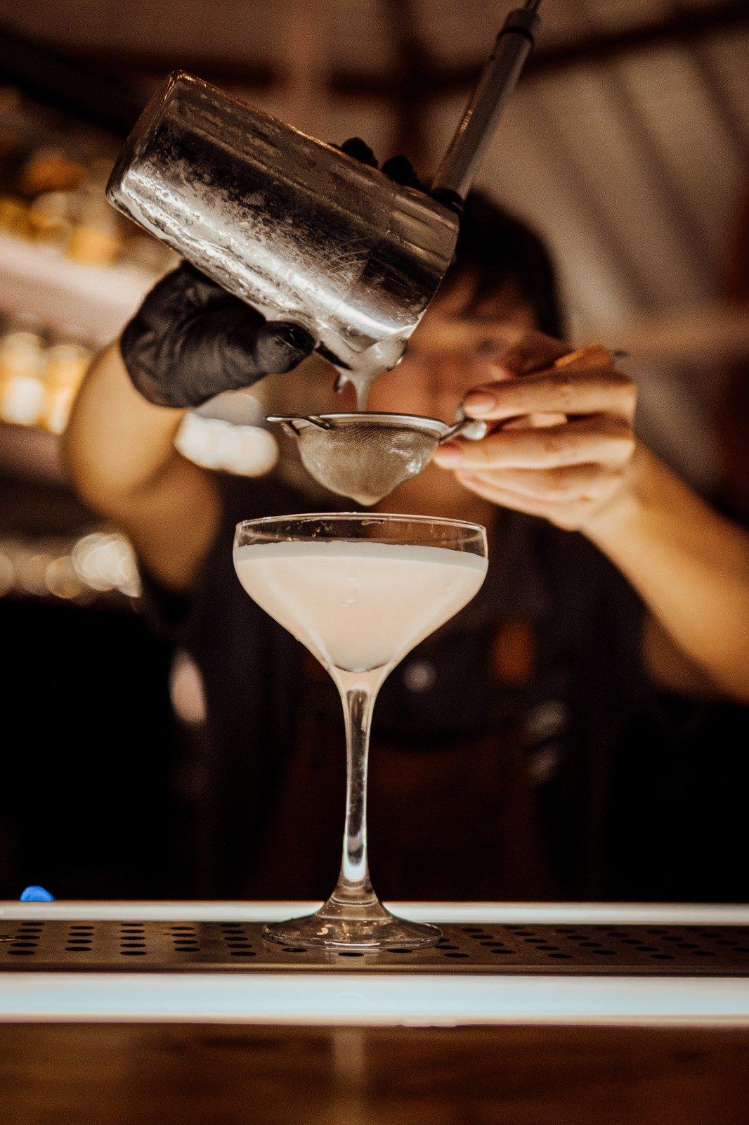 El bartender colando un trago en la copa, detrás de la barra