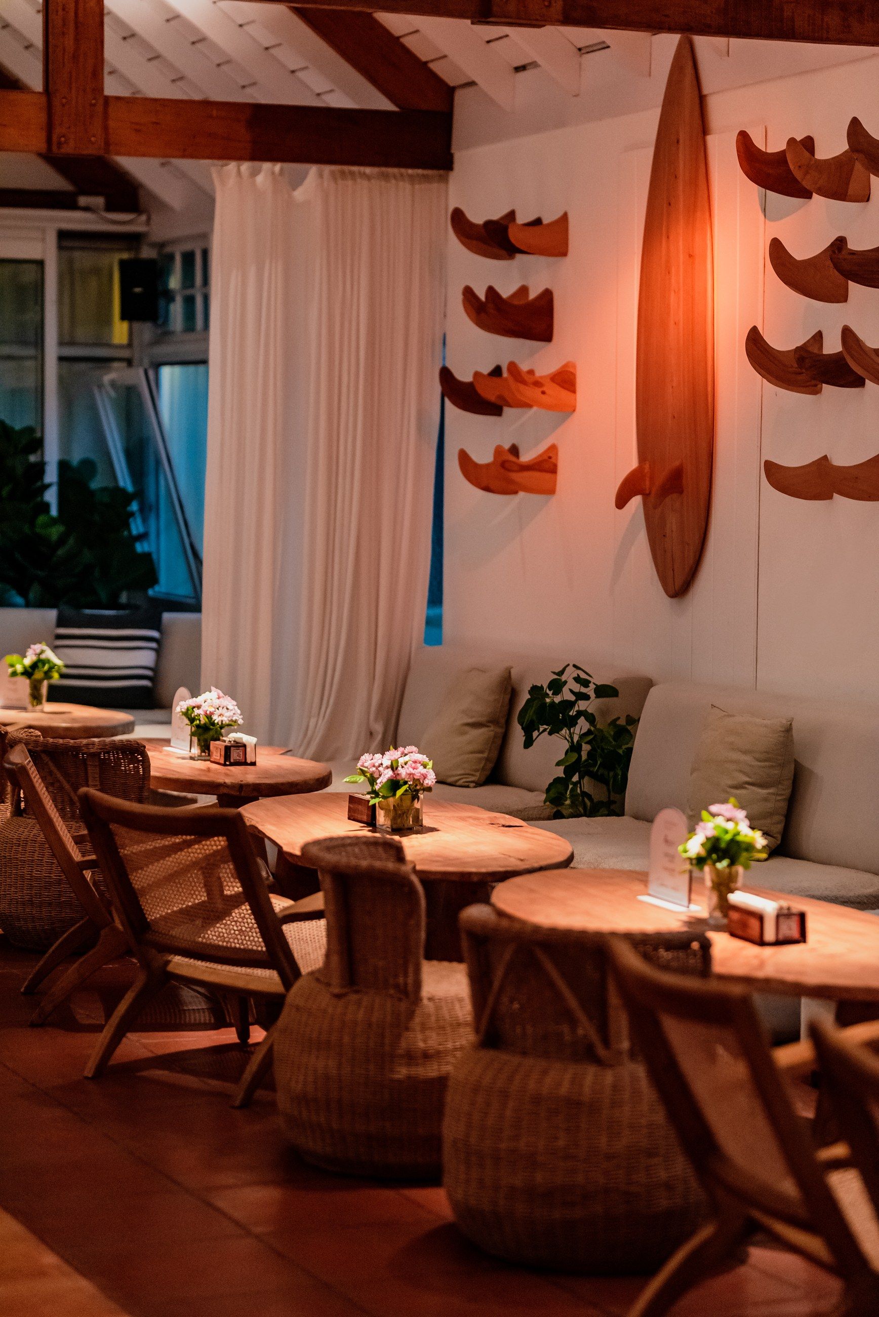 El sector lounge con las tablas de surf en la pared, mesas redondas de madera y flores