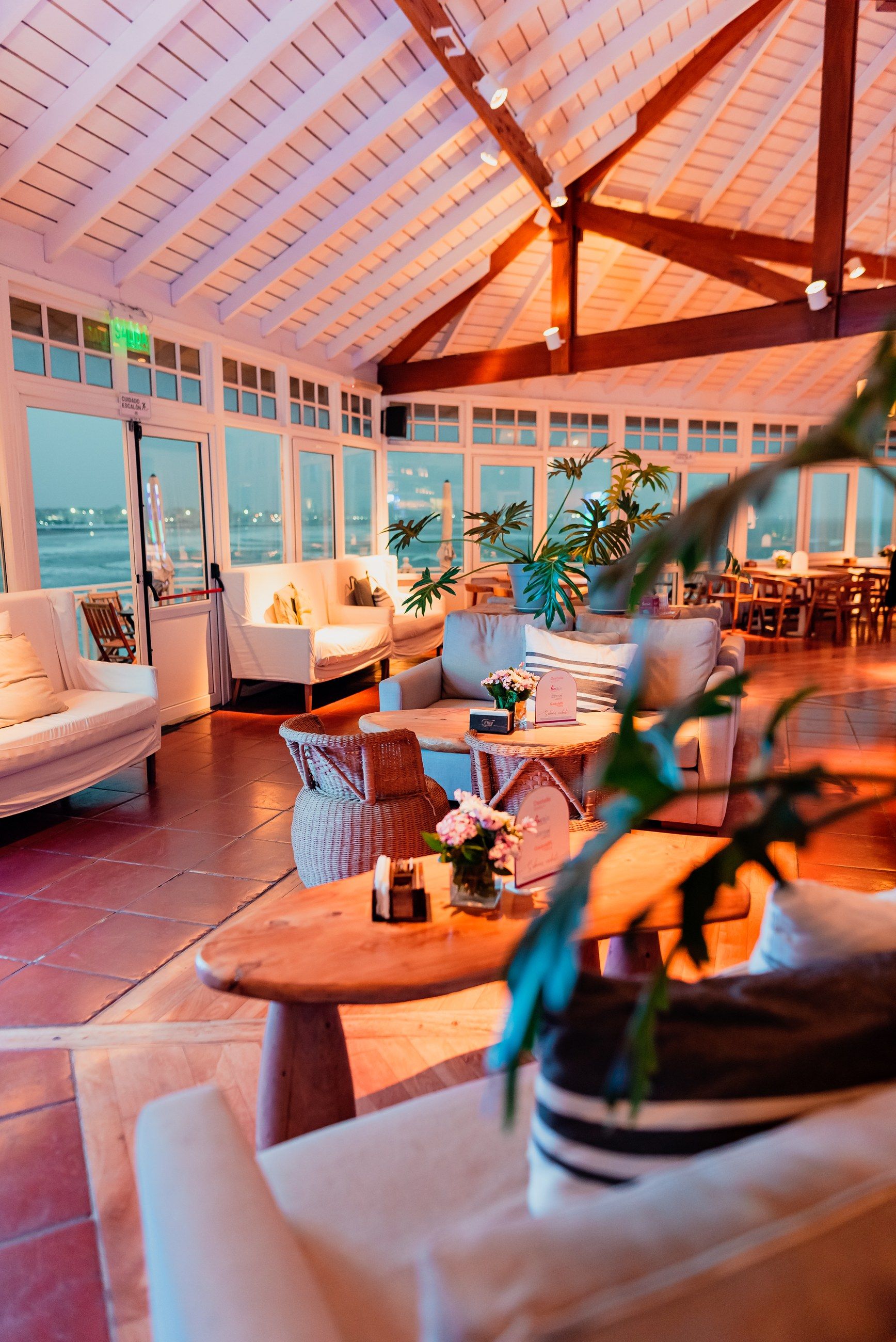El salón principal al atardecer, con el techo de madera a dos aguas, los sillones blancos y el mar por los ventanales