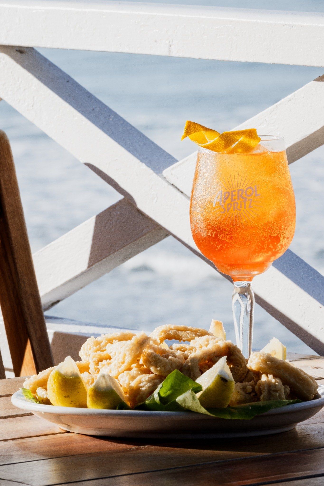 Un spritz y un plato de rabas con limón, sobre la mesa de la terraza frente al mar