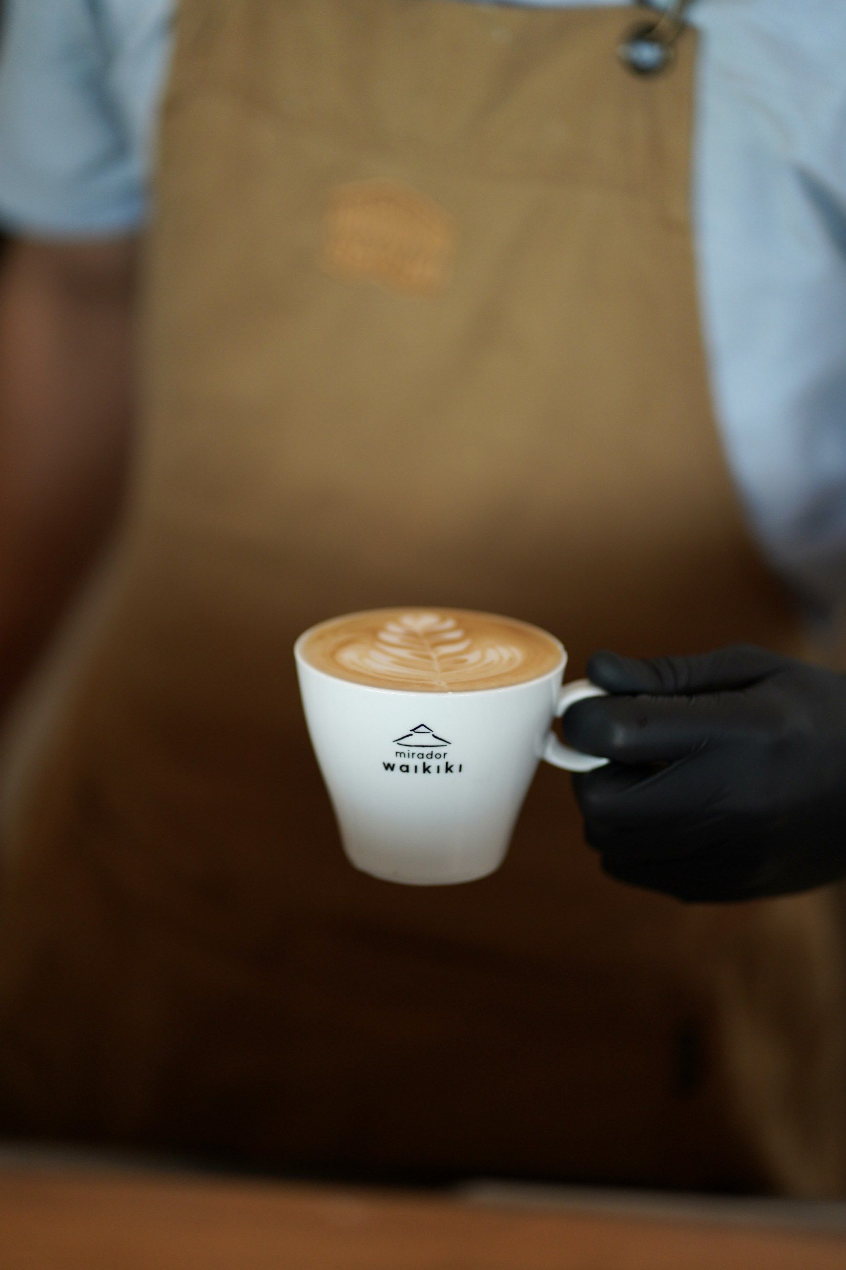 Una taza de café con leche con el logo de Mirador Waikiki, servida por el barista