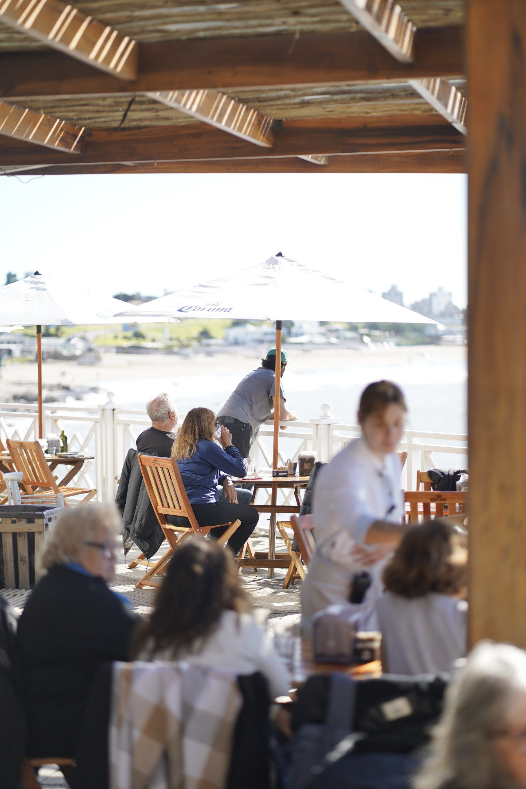 La terraza del restaurante llena a la hora del almuerzo, bajo los tejidos de macramé, con las sombrillas y el mar al fondo